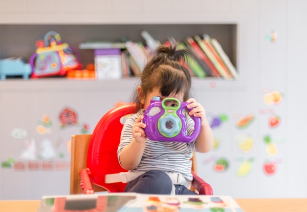 Toddler with toy camera in kindergarten